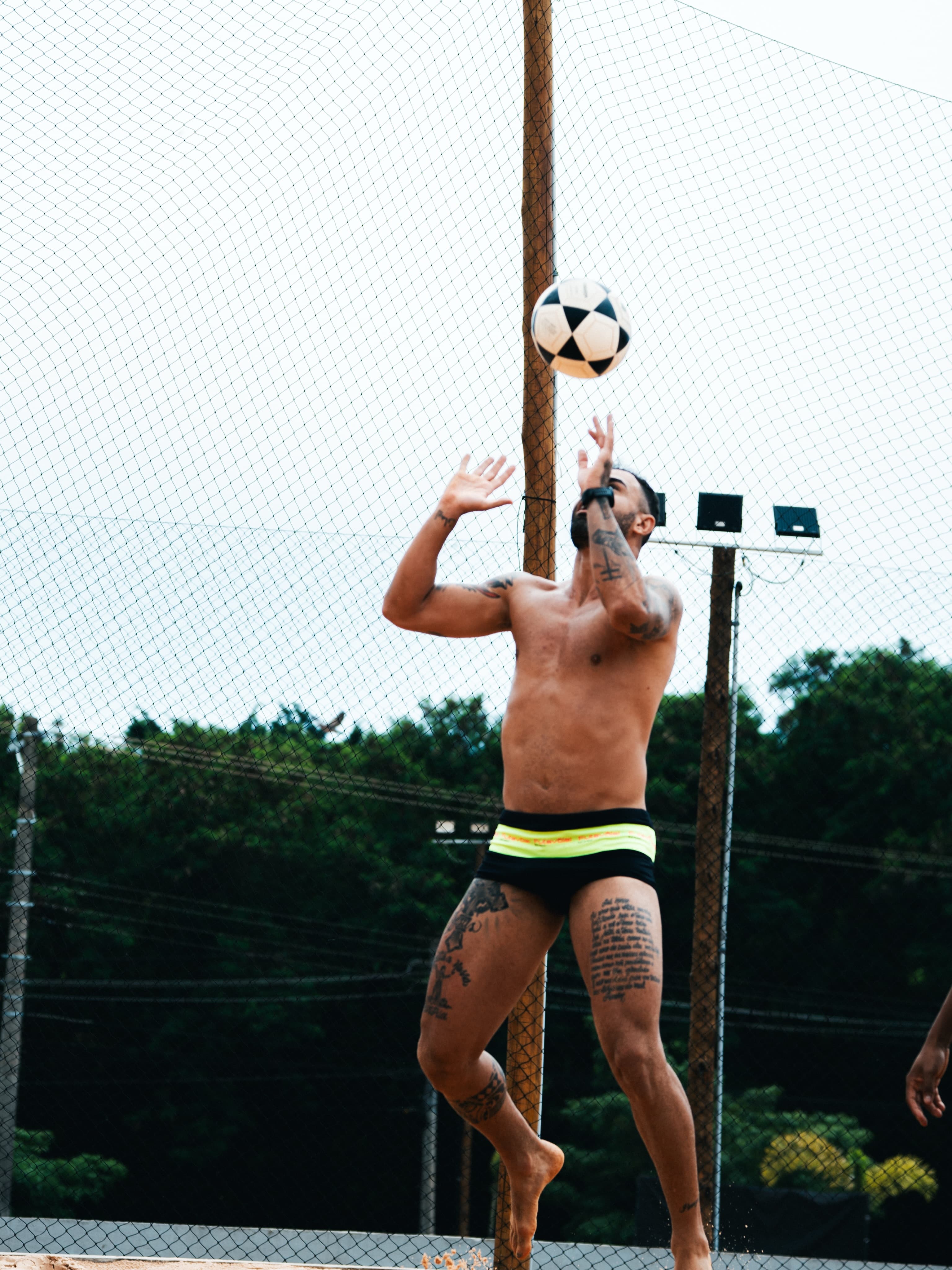 Jogador de futevôlei matando a bola no peito na quadra de areia, com a rede ao fundo