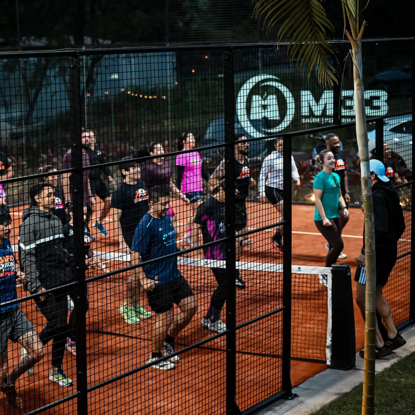 Grupo de corrida aquecendo na quadra de padel terracota, com o letreiro M33 no vidro