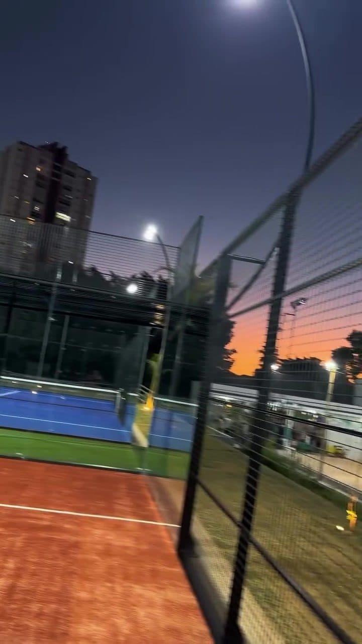 As duas quadras de padel, terracota e azul, com os refletores acesos no começo da noite